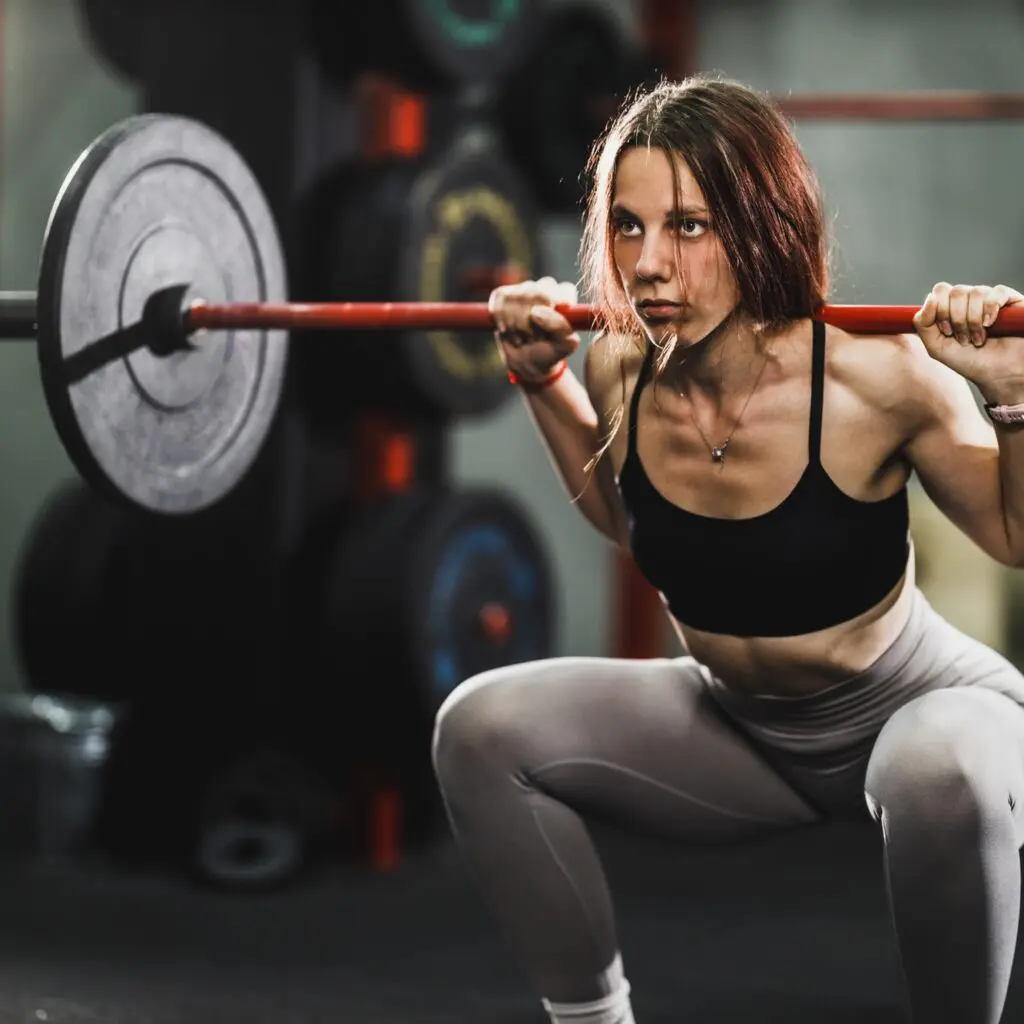 Muscular Woman Doing Squat Exercise With Barbell At The Gym